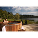 Couple enjoying a soak in their Cedar Hot Tub in the sun next to a lake