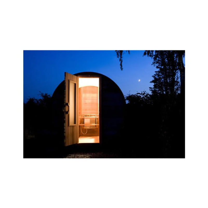 Northern Lights Red Cedar Barrel Sauna silhouetted at duck with open door showing lit interior 